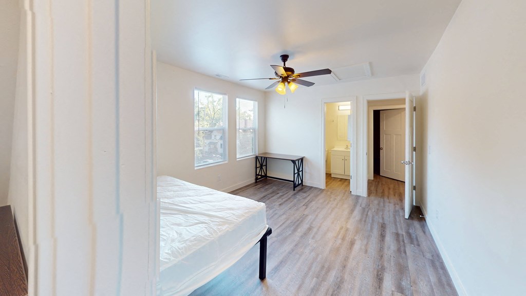 A bedroom with a bed, a ceiling fan, and a wooden floor.